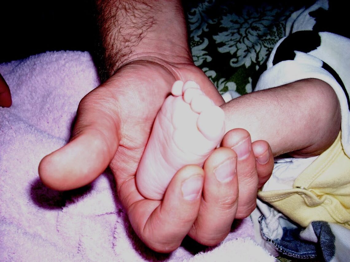 A photo of a father's hand close up gently cradling their infant's foot