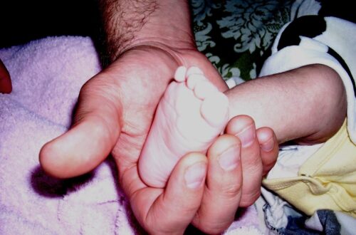A photo of a father's hand close up gently cradling their infant's foot