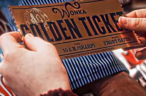 A shimmering "GOLDEN TICKET", the size of a large "Wonka Chocolate Bar" is held in the hands of an awestruck young boy named Charlie.