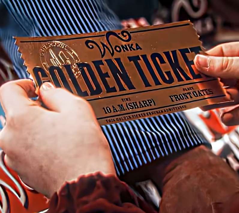 A shimmering "GOLDEN TICKET", the size of a large "Wonka Chocolate Bar" is held in the hands of an awestruck young boy named Charlie.